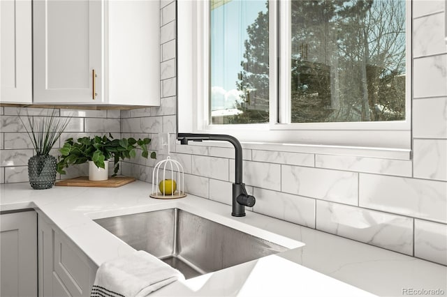 interior details featuring light stone countertops, white cabinetry, decorative backsplash, and sink