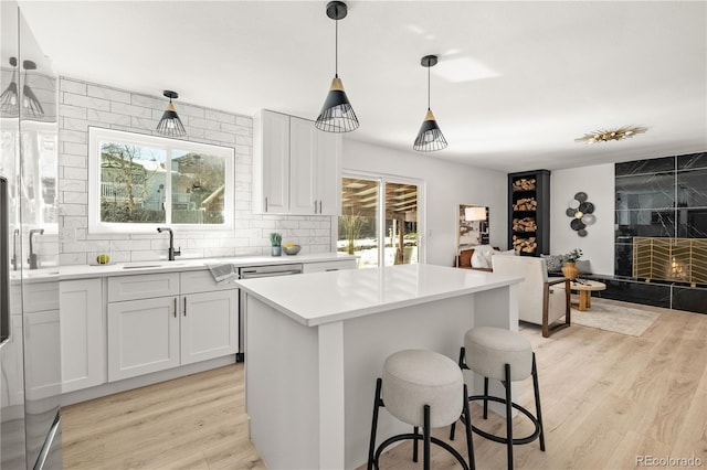 kitchen with pendant lighting, white cabinets, a center island, light hardwood / wood-style floors, and backsplash