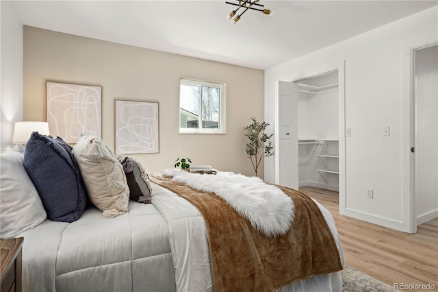 bedroom featuring a walk in closet, a closet, a chandelier, and light hardwood / wood-style floors