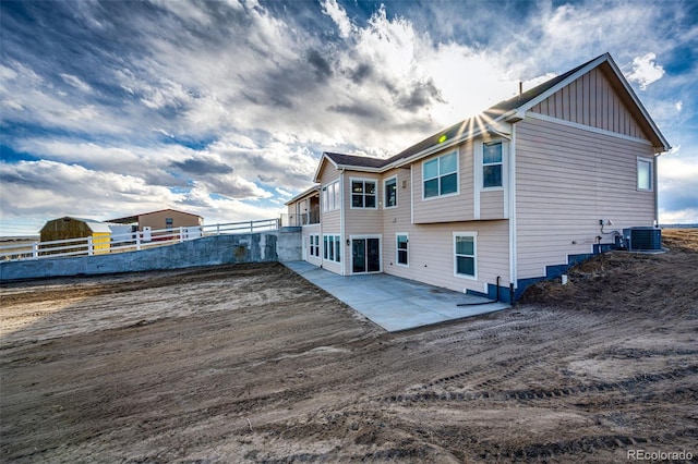 rear view of property featuring board and batten siding, a patio area, fence, and central AC