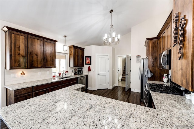 kitchen featuring dark brown cabinetry, dark wood-style floors, appliances with stainless steel finishes, light stone counters, and backsplash