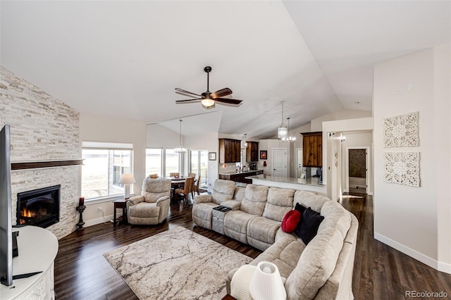 living area with baseboards, lofted ceiling, ceiling fan, dark wood-type flooring, and a stone fireplace