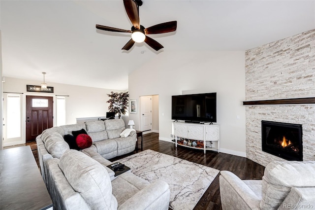 living room featuring dark wood-style flooring, lofted ceiling, ceiling fan, a stone fireplace, and baseboards