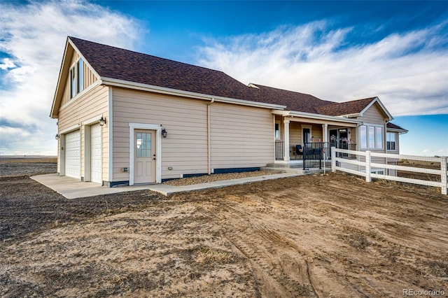 view of front of property featuring a garage, covered porch, fence, and roof with shingles