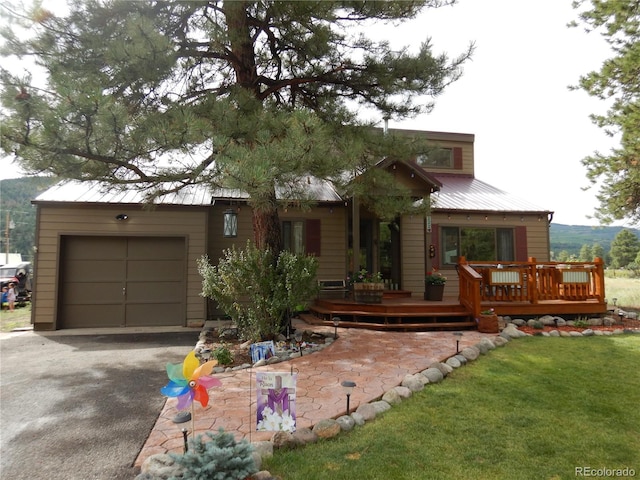 chalet / cabin featuring aphalt driveway, an attached garage, metal roof, a deck, and a front lawn