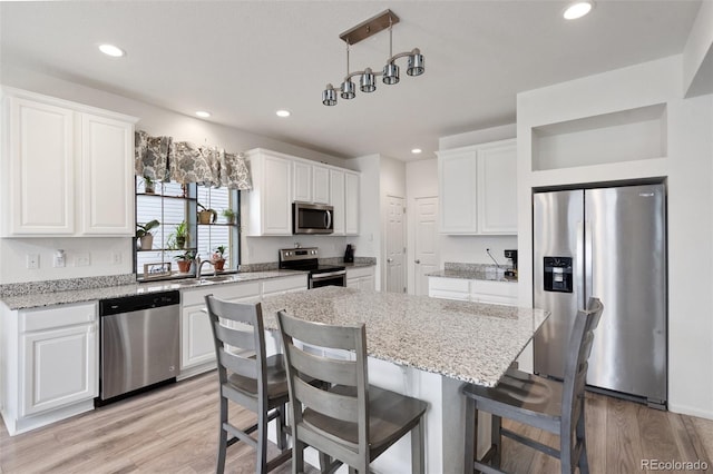 kitchen featuring a kitchen island, pendant lighting, white cabinetry, light stone countertops, and stainless steel appliances