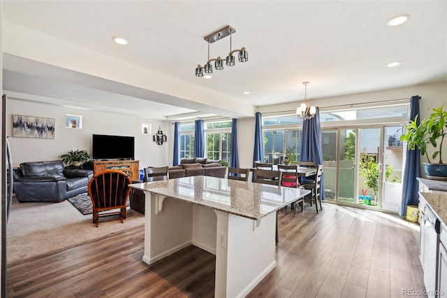 kitchen with dark wood-type flooring, hanging light fixtures, light stone countertops, a kitchen island, and a breakfast bar