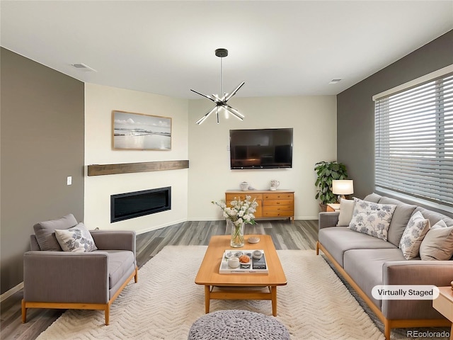 living room with a notable chandelier, visible vents, wood finished floors, and a glass covered fireplace