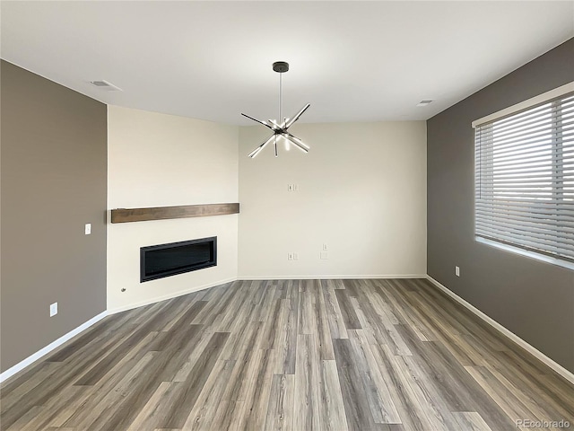 unfurnished living room featuring baseboards, visible vents, a glass covered fireplace, wood finished floors, and a chandelier