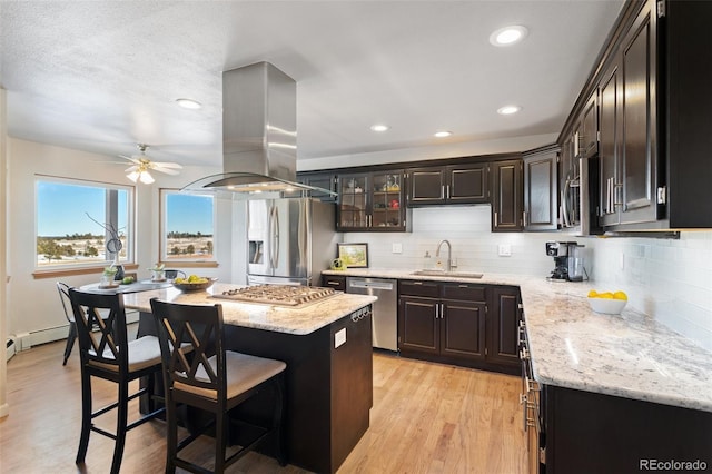 kitchen with island range hood, light wood-style flooring, appliances with stainless steel finishes, a sink, and backsplash