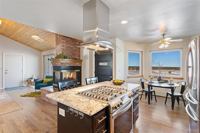 kitchen with appliances with stainless steel finishes, vaulted ceiling, light wood-style flooring, and island exhaust hood