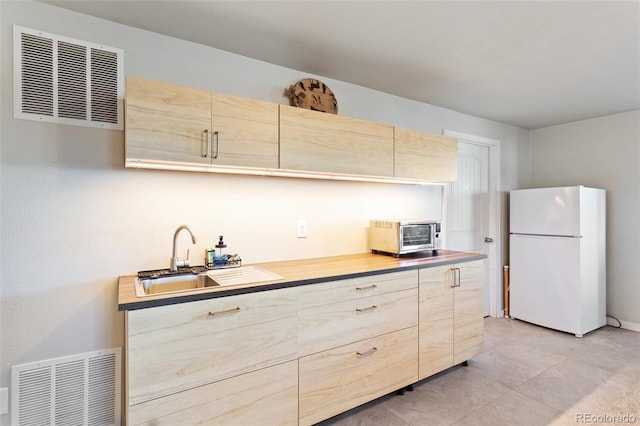 kitchen with visible vents, light brown cabinets, and freestanding refrigerator