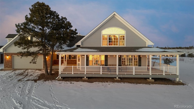 snow covered back of property featuring an attached garage and a porch