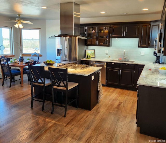 kitchen with light stone counters, light wood-style flooring, a sink, appliances with stainless steel finishes, and island exhaust hood