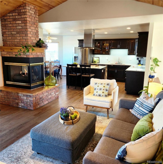 living room featuring lofted ceiling, a brick fireplace, light wood-style flooring, and recessed lighting