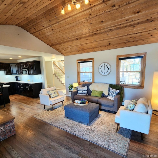 living area with a wealth of natural light, wood finished floors, vaulted ceiling, and stairs