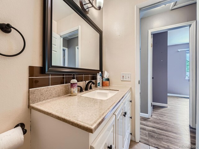 12991 E Idaho Dr, Aurora, CO 80012 - bathroom featuring decorative backsplash, vanity, wood finished floors, and baseboards