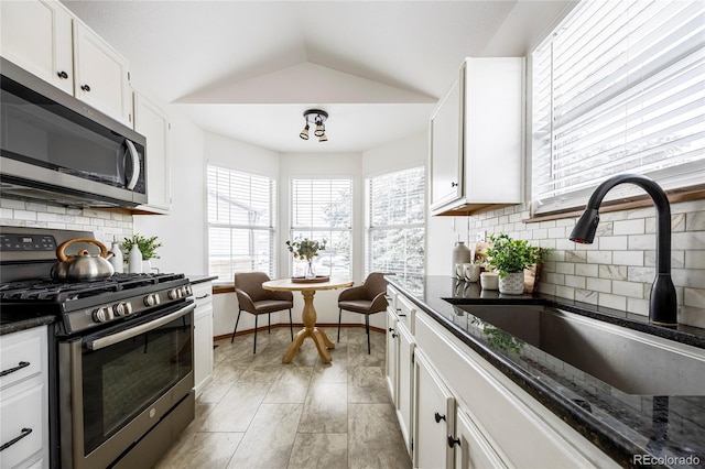 kitchen featuring appliances with stainless steel finishes, dark stone counters, vaulted ceiling, sink, and white cabinetry