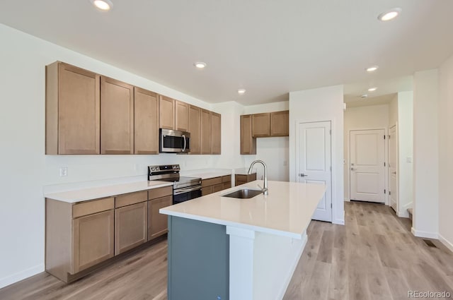 kitchen featuring appliances with stainless steel finishes, light wood-type flooring, a center island with sink, and sink