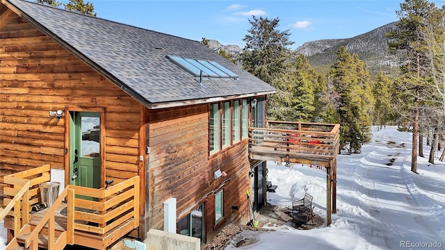 view of snow covered exterior with roof with shingles and a mountain view