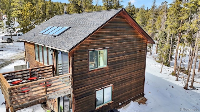 snow covered property with a wooded view, roof with shingles, and log veneer siding