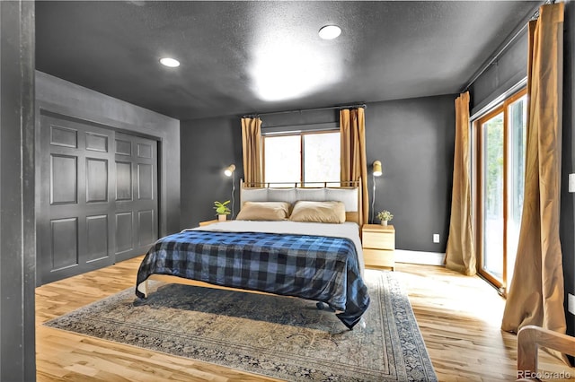 bedroom with a closet, a textured ceiling, baseboards, and wood finished floors