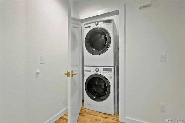 washroom featuring stacked washing maching and dryer, baseboards, laundry area, and light wood finished floors