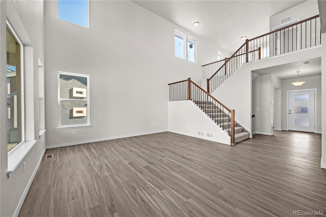 unfurnished living room featuring visible vents, dark wood finished floors, baseboards, a towering ceiling, and stairway