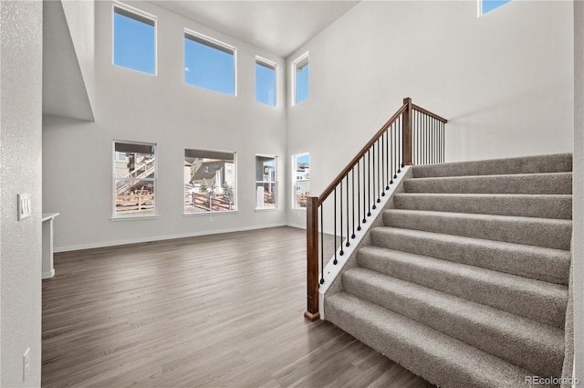 staircase featuring a high ceiling, baseboards, and wood finished floors