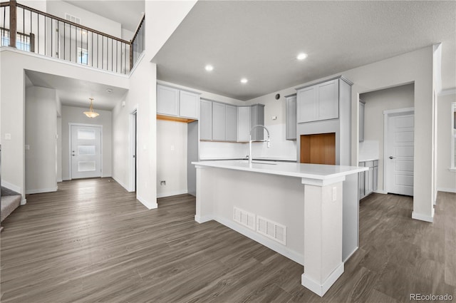 kitchen with visible vents, dark wood-style floors, a kitchen island with sink, light countertops, and a sink