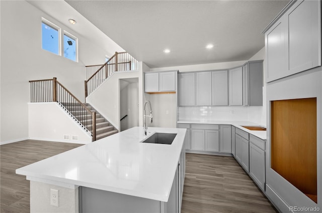 kitchen featuring gray cabinets, light countertops, a center island with sink, and a sink