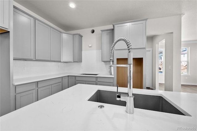 kitchen with light stone countertops, decorative backsplash, a sink, and gray cabinetry