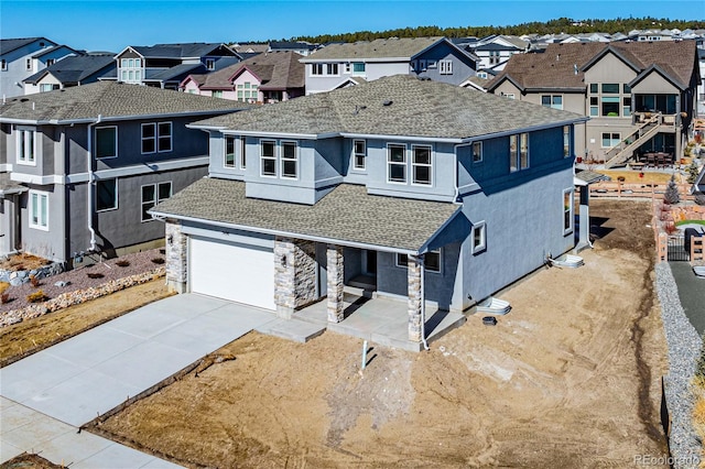 view of front facade with a shingled roof, concrete driveway, stone siding, a residential view, and stucco siding