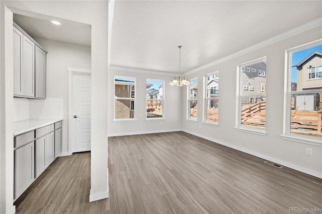 unfurnished dining area with baseboards, a notable chandelier, visible vents, and wood finished floors