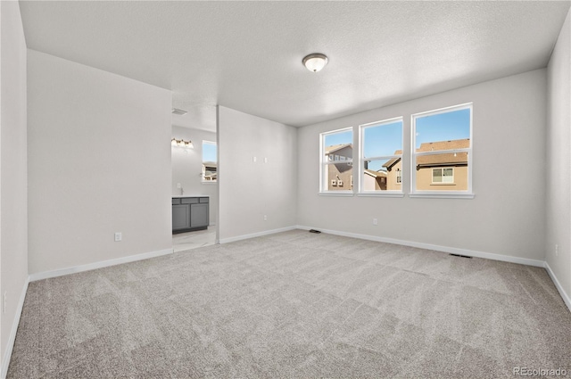 empty room with baseboards, a textured ceiling, and light colored carpet