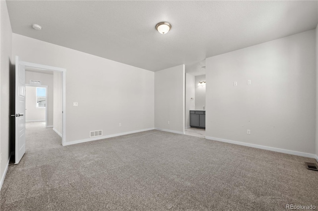 spare room with light carpet, baseboards, and a textured ceiling