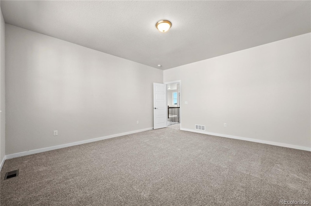 unfurnished room with a textured ceiling, carpet floors, visible vents, and baseboards