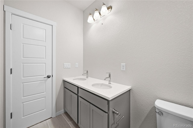 bathroom with a textured wall, double vanity, a sink, and toilet