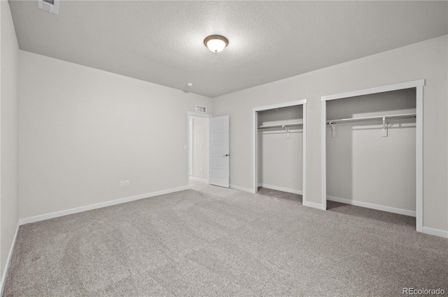 unfurnished bedroom with carpet floors, multiple closets, visible vents, a textured ceiling, and baseboards