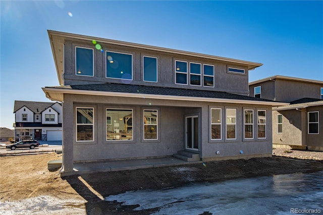 rear view of house featuring entry steps, a shingled roof, and stucco siding