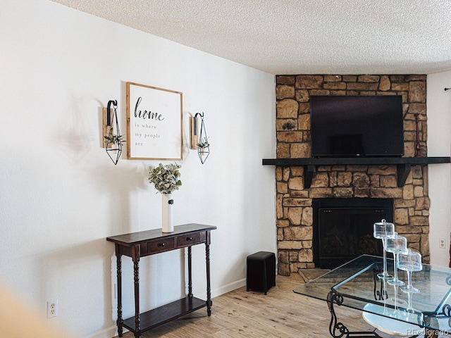 living area with a textured ceiling, wood finished floors, baseboards, and a fireplace
