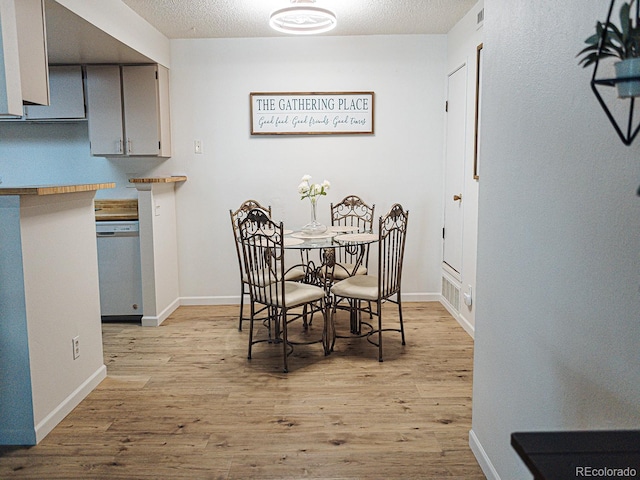 dining space with baseboards, visible vents, light wood-type flooring, and a textured ceiling