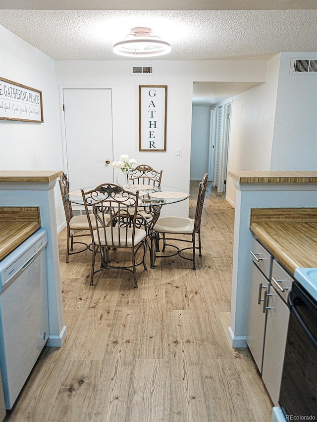 dining area with light wood-style floors, visible vents, and a textured ceiling
