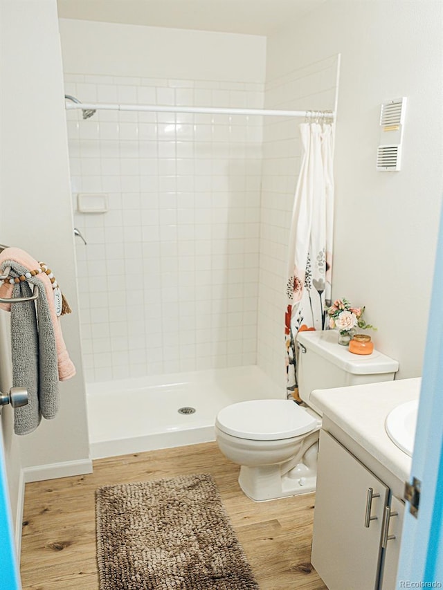 full bathroom with toilet, wood finished floors, a tile shower, visible vents, and vanity