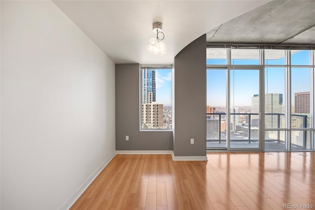 spare room featuring light hardwood / wood-style flooring, a wall of windows, and an inviting chandelier