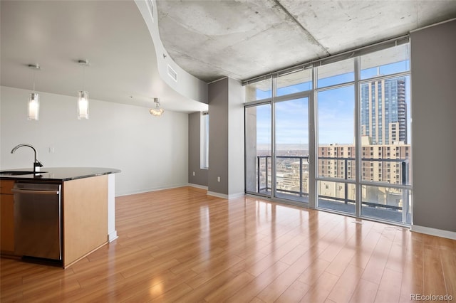 kitchen featuring sink, decorative light fixtures, stainless steel dishwasher, a wall of windows, and light hardwood / wood-style floors