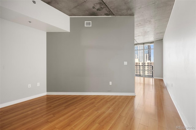 spare room with a wall of windows and light hardwood / wood-style floors