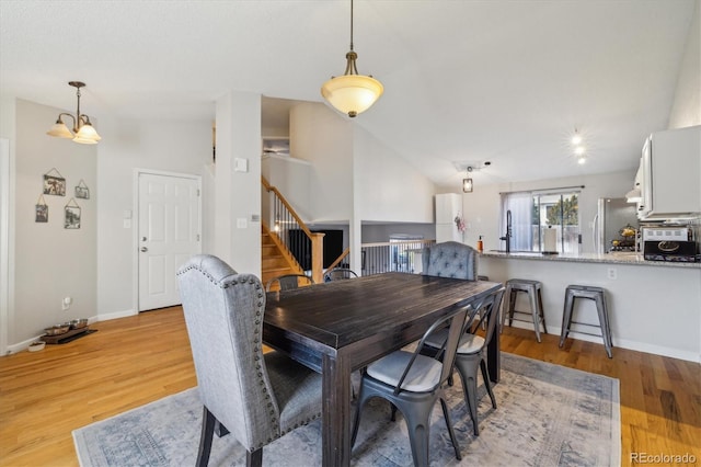 dining room with light wood-type flooring, lofted ceiling, and sink