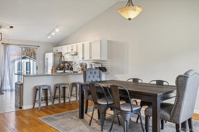 dining room with light wood-style floors and high vaulted ceiling