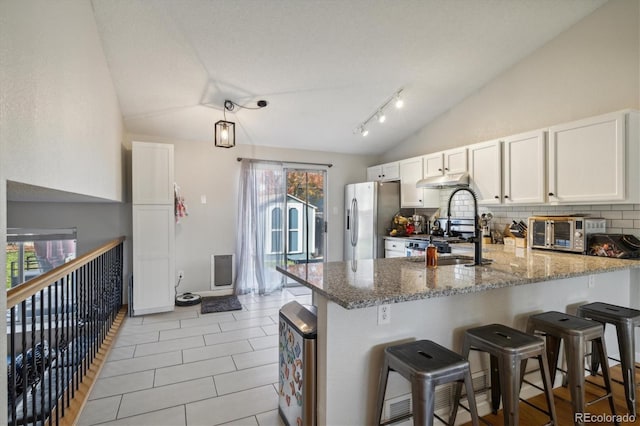 kitchen with a peninsula, a sink, white cabinets, vaulted ceiling, and stainless steel fridge